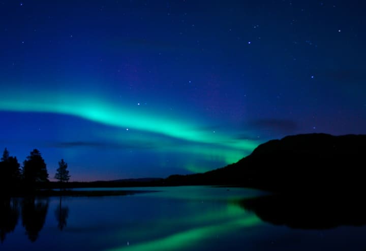 Arc vert d’aurores boréales se reflétant dans un lac nordique immobile par nuit claire
