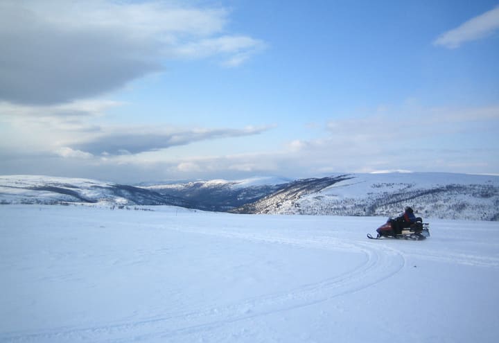 Motoneige traversant la neige vierge du plateau du Finnmark au-dessus d’Alta sous un ciel bleu