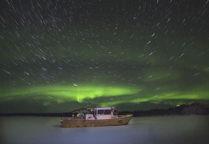 Star trails and a faint aurora over frozen Lake Inari on a clear winter night