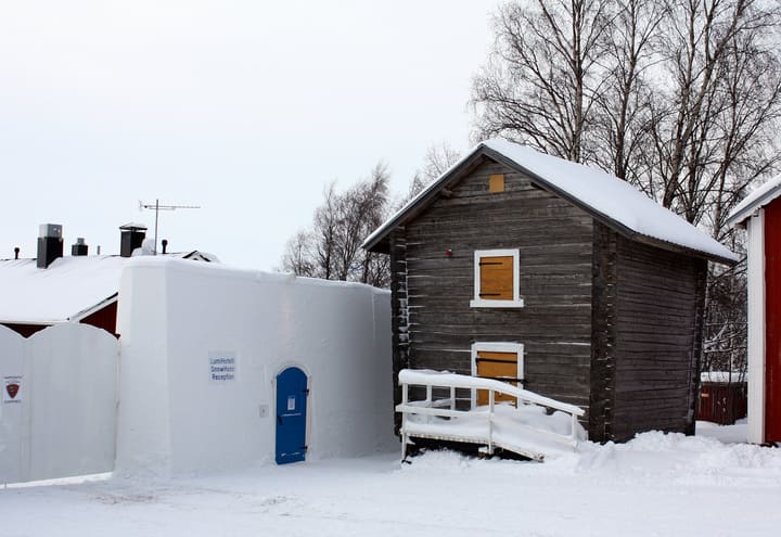 Schneemauer des Kemi SnowCastle neben einem traditionellen Holzhaus im Winter