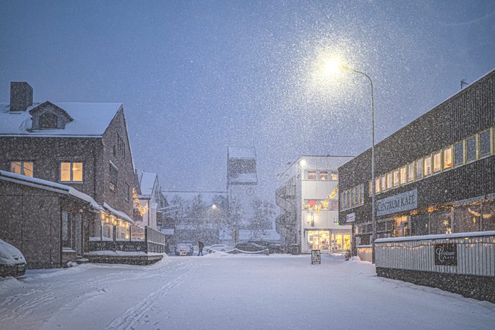 Snow falling on a Kirkenes town street with lights and the church in December 2019