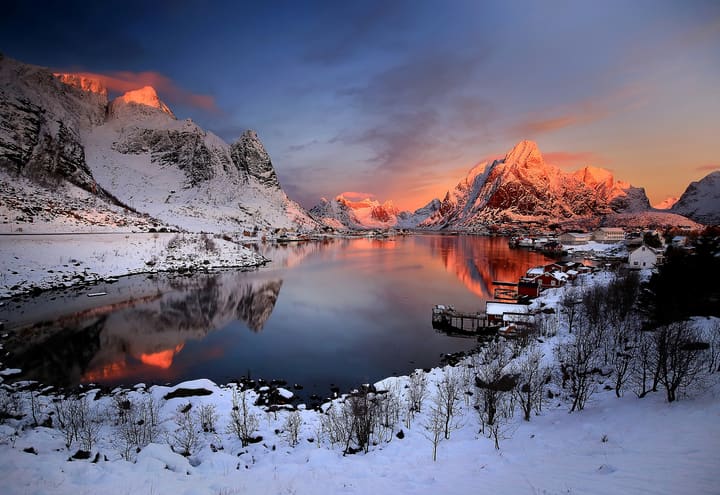 Winter sunrise lighting the mountain tops above Reine and its snow-covered shore