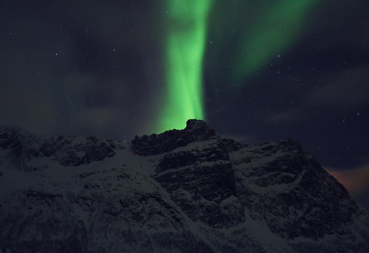 Green northern lights arc above a snow-covered mountain ridge near Tromsø