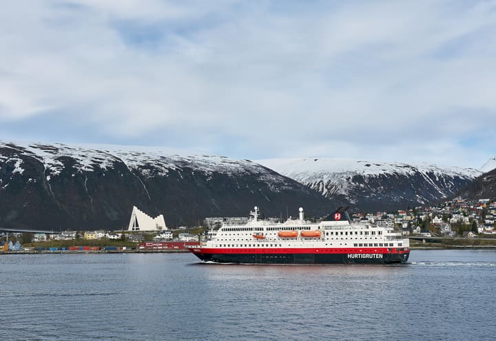 Coastal ship leaving Tromsø harbour in winter with the Arctic Cathedral and snow-covered mountains behind