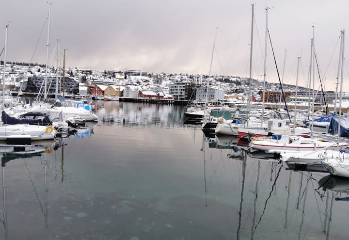 Small boats moored in Tromsø harbour under snow-dusted hills on a grey winter day