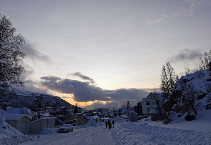 Snow-covered residential street in Tromsø at dusk during the short winter day